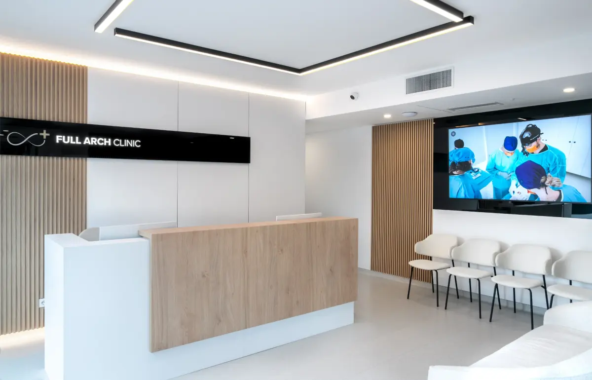 Recepția Full Arch Clinic, cu zona de așteptare și ecranul pe care rulează imagini din sala de intervenții